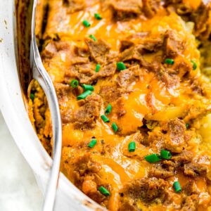Zoomed in photo of a cheesy casserole in a white ceramic baking dish with a spatula sticking into the side