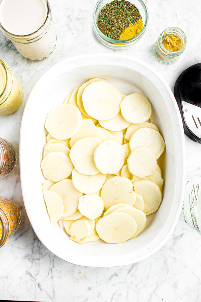 Overhead photo of thinly sliced potatoes arranged in a layer in a baking dish