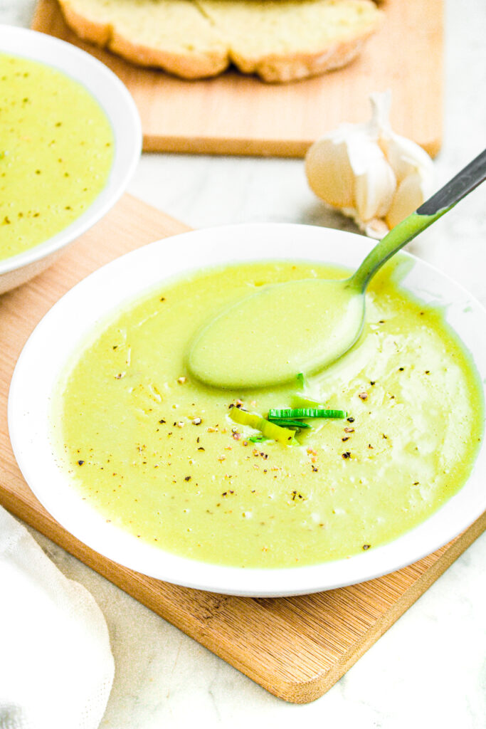 Overhead view of a round white bowl with creamy potato leek soup and a spoon digging into it
