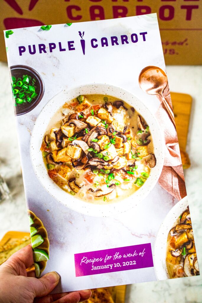 A hand holding a Purple Carrot recipe booklet that comes with their meal delivery boxes.