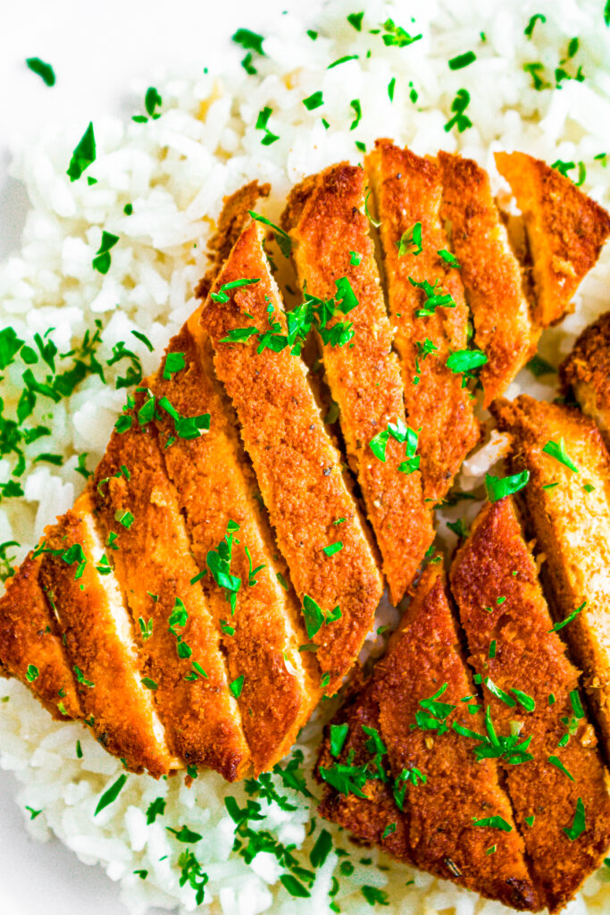 Overhead view of a red curry tofu cutlet sliced on a bias sitting on a bed of basmati rice sprinkled with parsley