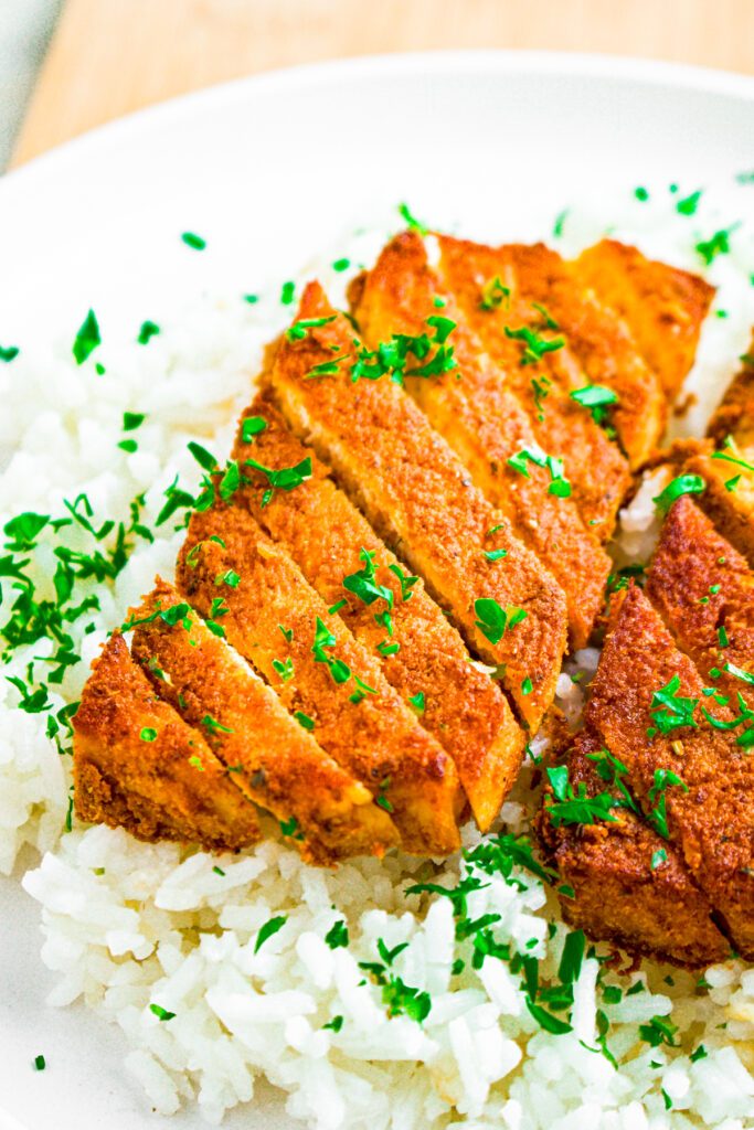 Head on view of a vegan curry tofu cutlet sliced diagonally on a bed of white rice sprinkled with parsley
