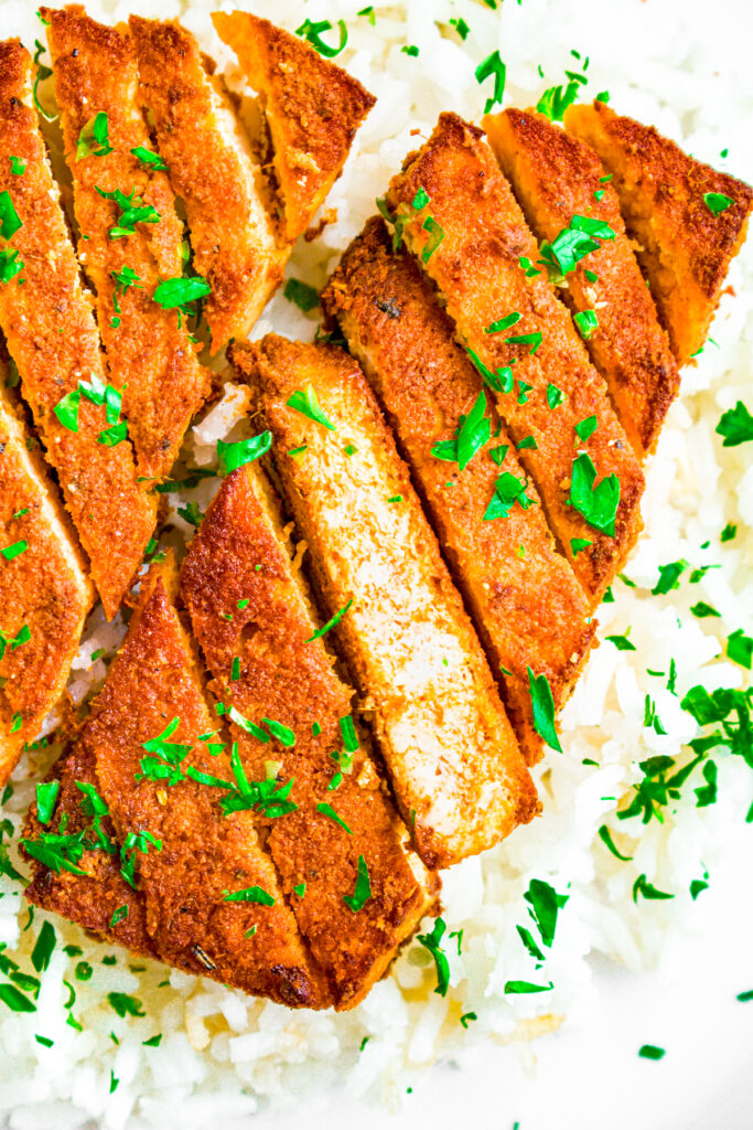 Overhead close up view of a curried tofu cutlet sliced on a bias sitting on a bed of basmati rice sprinkled with parsley