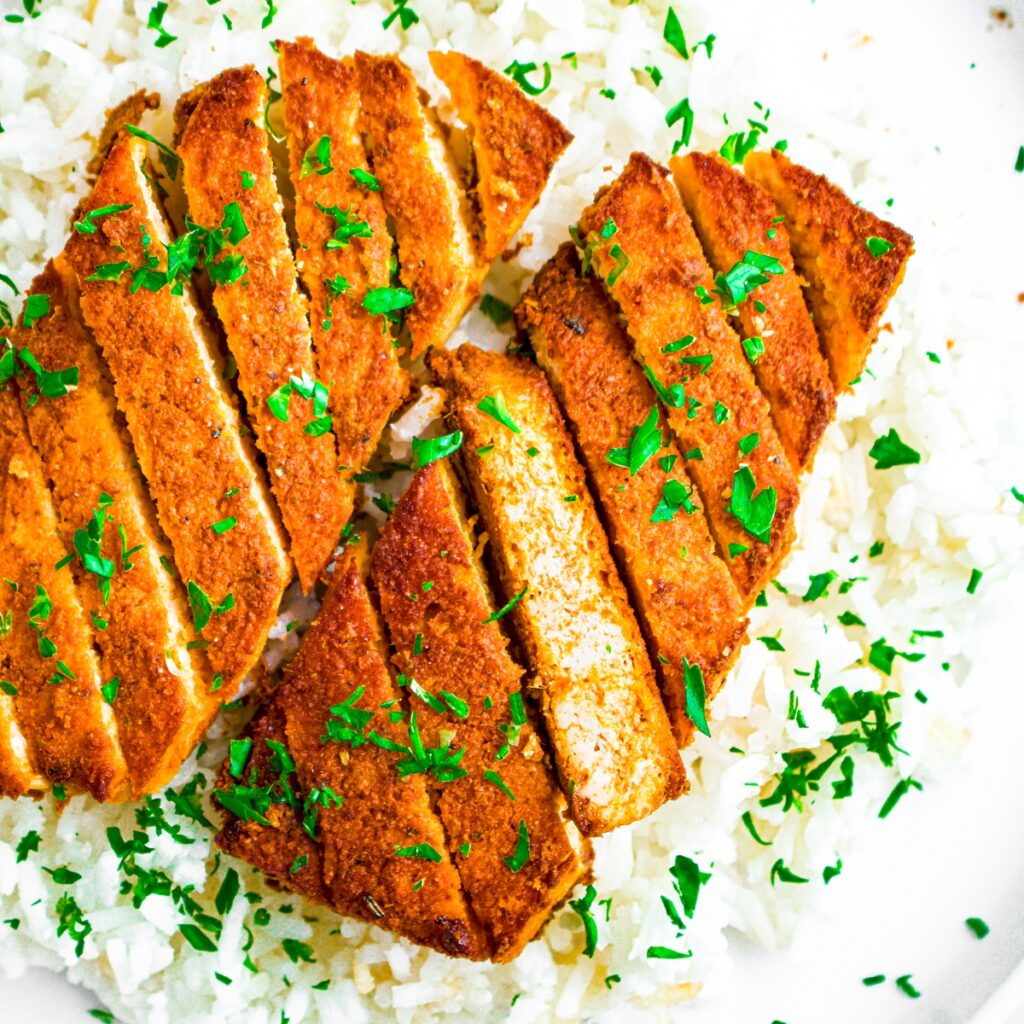 Overhead view of a red curry tofu cutlet sliced on a bias sitting on a bed of basmati rice sprinkled with parsley