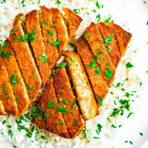 Overhead view of a red curry tofu cutlet sliced on a bias sitting on a bed of basmati rice sprinkled with parsley