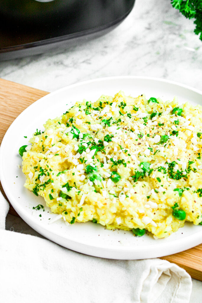 Overhead view of a round white view on a wooden plank piled high with rice cooker risotto with peas