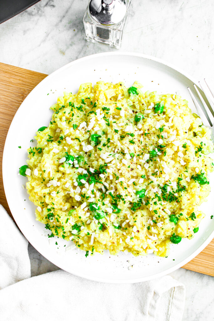 Overhead view of a round white plate on a wood plank piled high with dairy free risotto with peas and herbs
