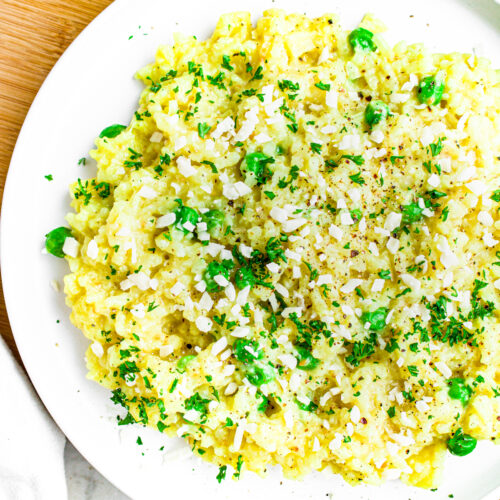 Overhead close up view of a round white plate of vegan risotto with peas and herbs next to a clear pepper shaker