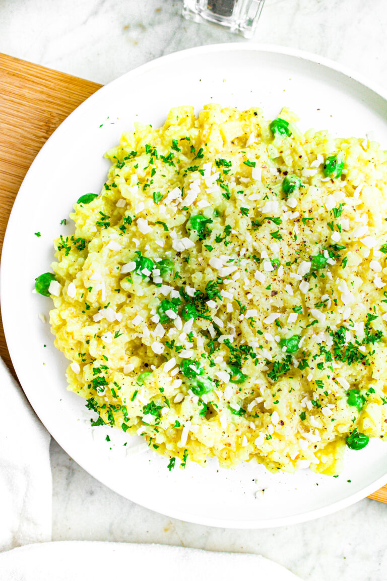 Overhead close up view of a round white plate of vegan risotto with peas and herbs next to a clear pepper shaker