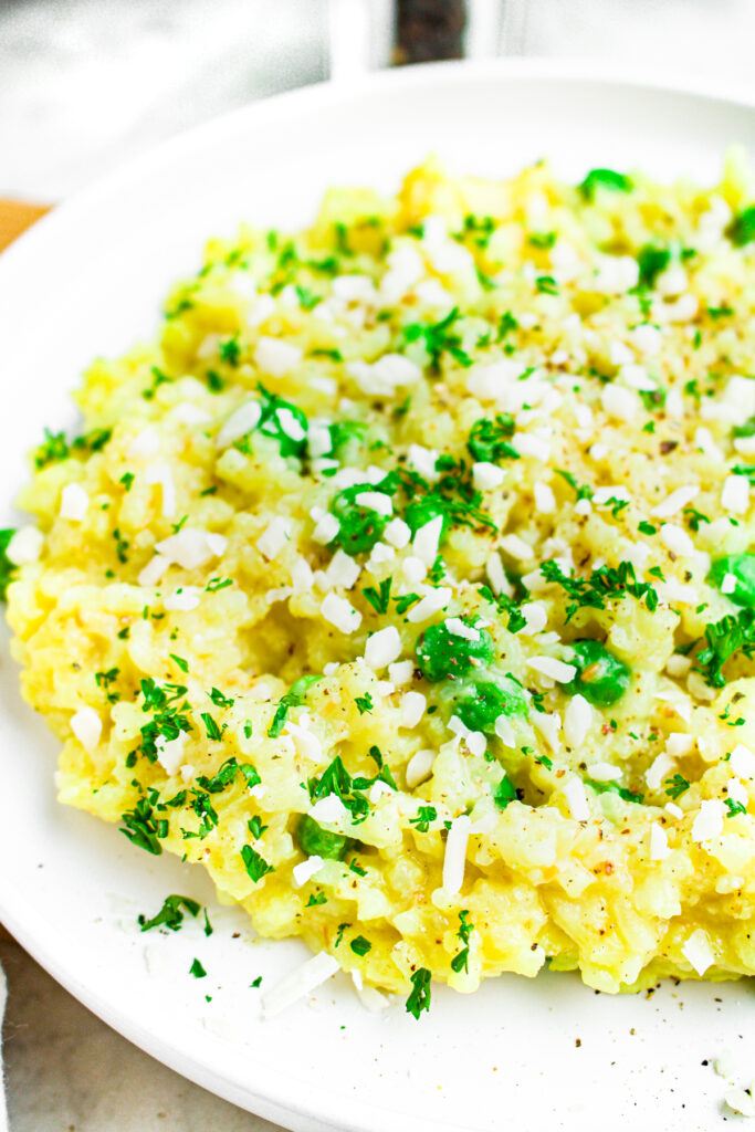 Close up head on view of a round white plate of creamy vegetarian risotto made in a rice cooker and topped with minced parsley
