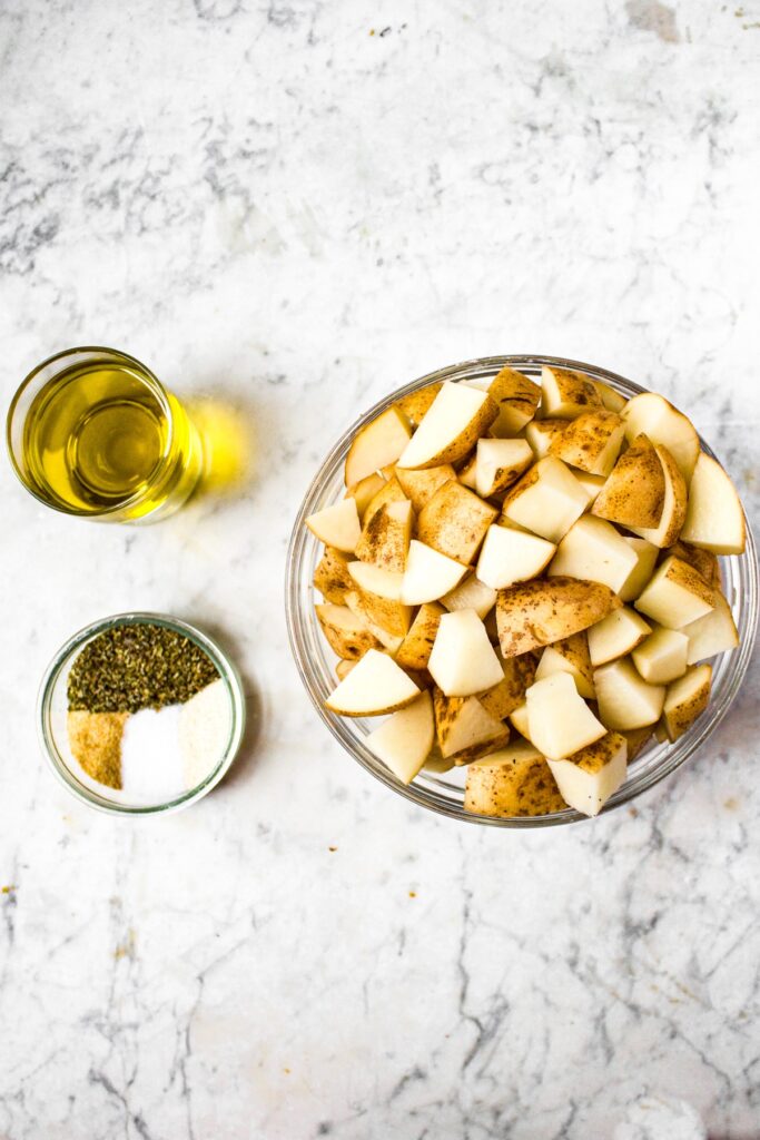 Overhead shot of the ingredients you need to make classic roasted potatoes: diced russet potatoes, olive oil, salt, onion powder, garlic powder, and Italian seasoning.
