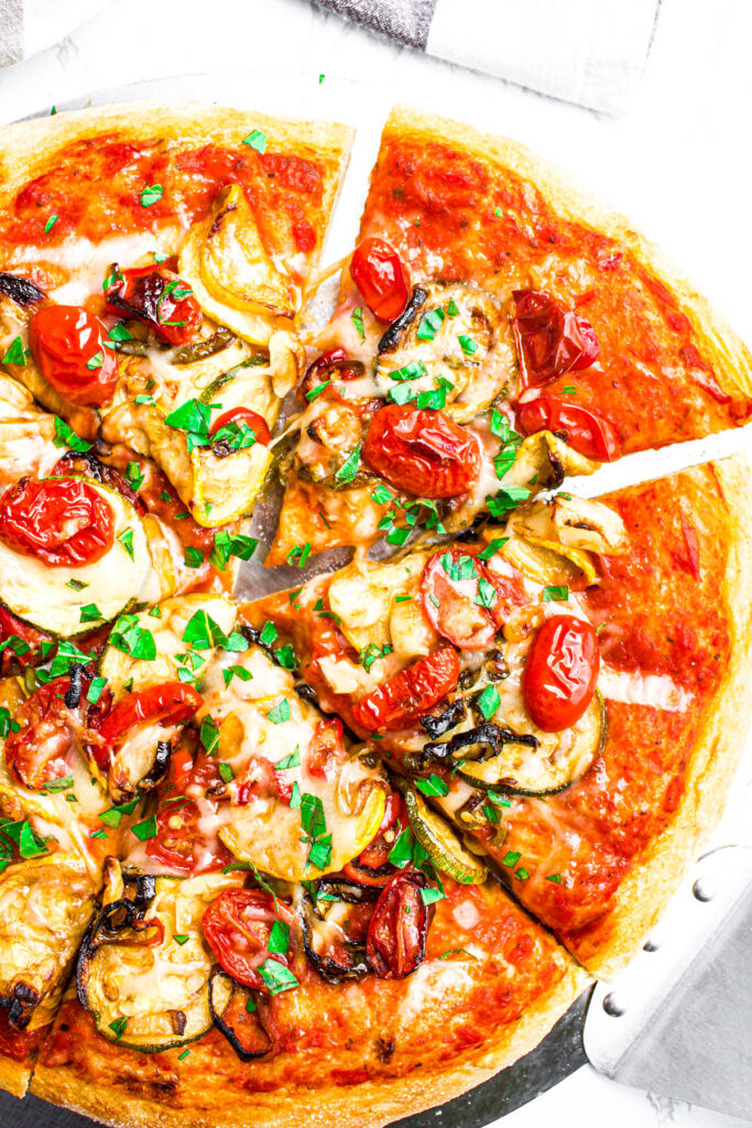 Overhead view of a sliced air fried veggie pizza with the slice in the top right corner pulled out