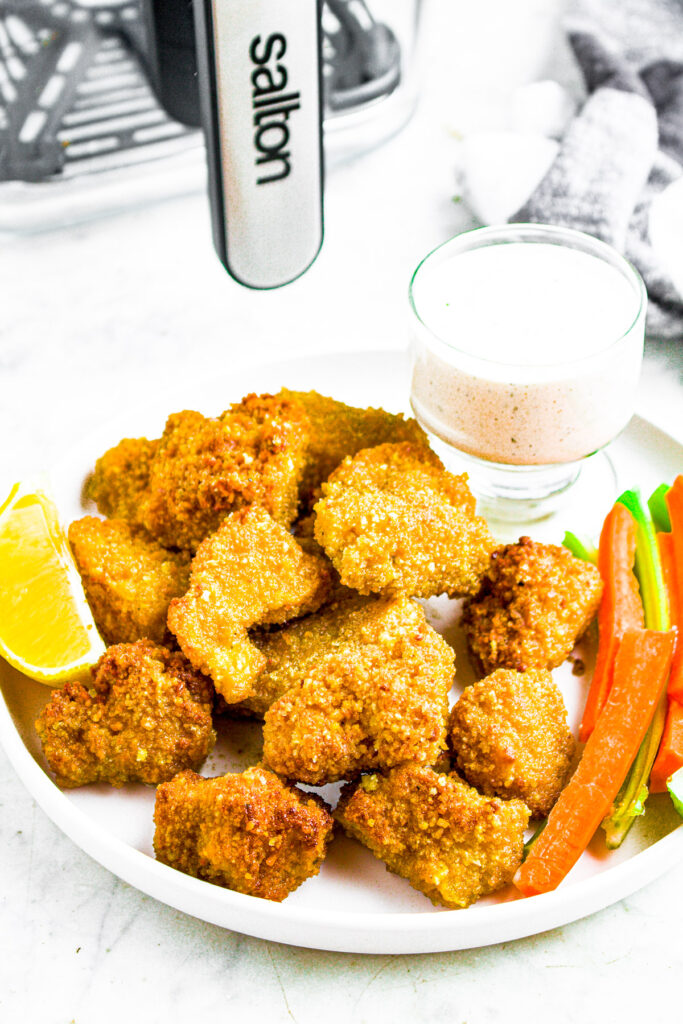 Overhead photo of a plate of lemon pepper tofu wings on a round white plate with a lemon wedge, carrots, celery, and a Salton air fryer inthe background