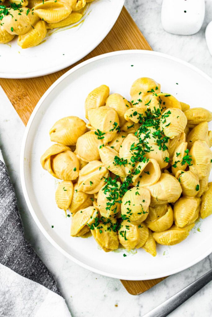 Overhead shot of a round white plate piled high with medium shell pasta in a creamy cheesy sauce sprinkled with fresh minced herbs