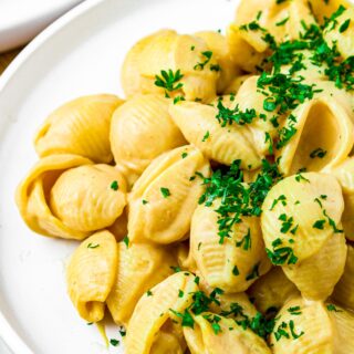 Overhead close up shot of a pile of nut-free vegan shells and cheese sprinkled with minced fresh herbs