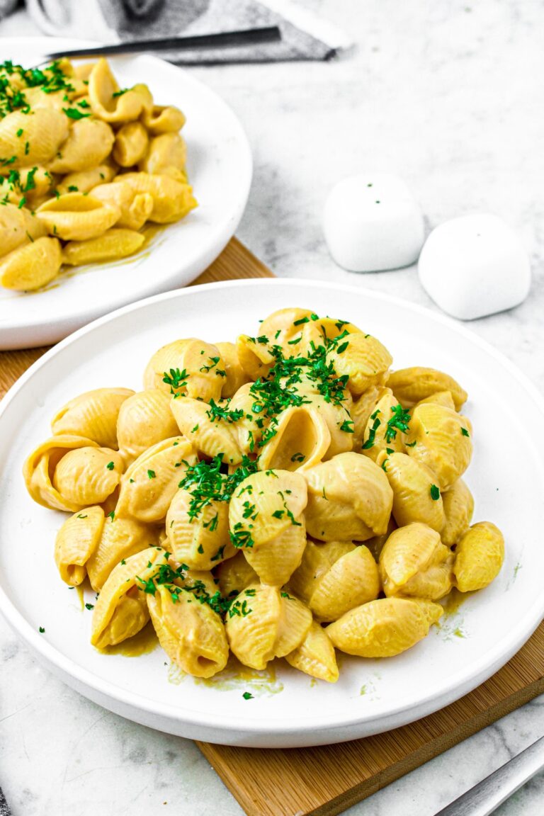 Overhead shot of a round white plate with a pile of vegan shells and cheese sprinkled with fresh minced parsley