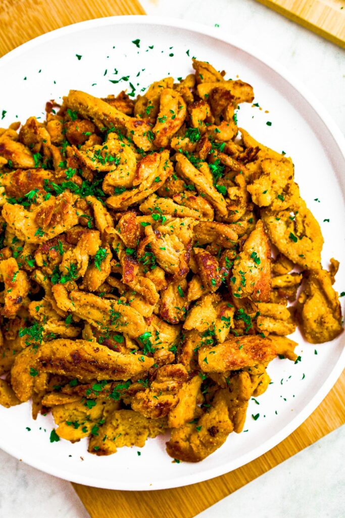 Overhead photo of pan-friend soy curls on a round white plate topped with minced fresh parsley