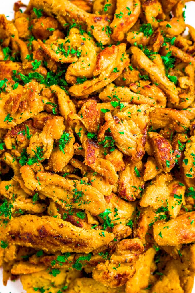 Close up photo of seared soy curls sprinkled with bright green flecks of parsley