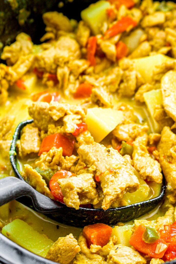 Zoomed in photo of a ladle scooping creamy soy curl curry out of a crockpot