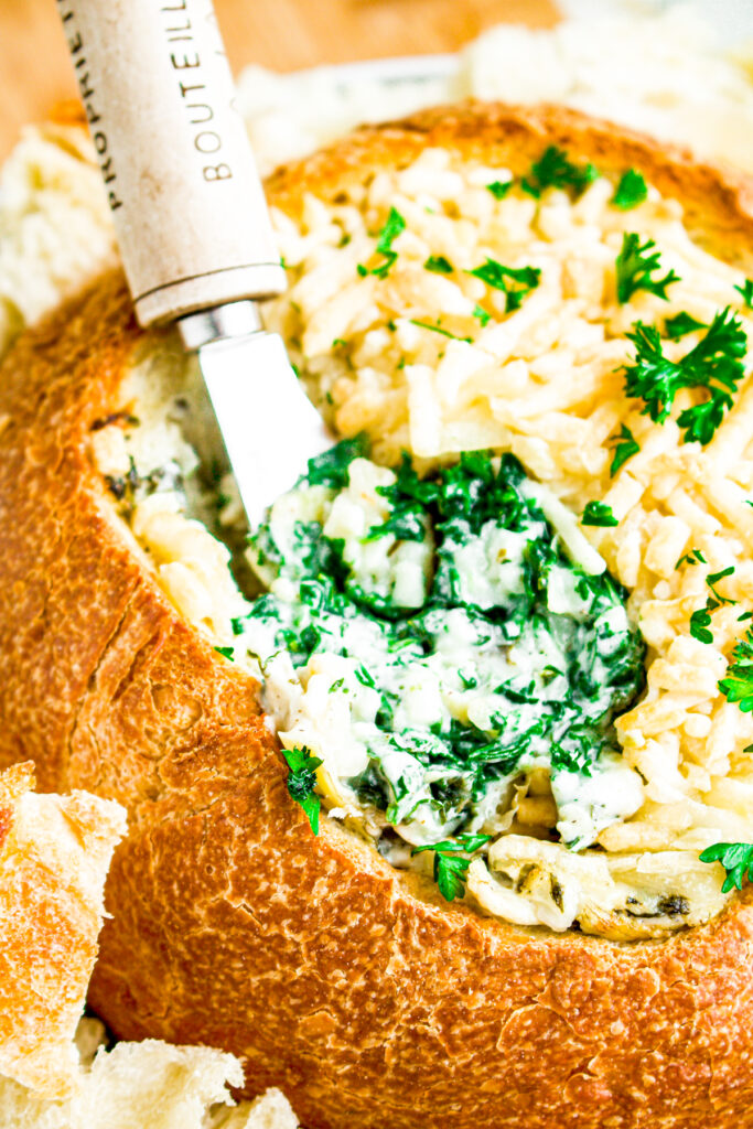 Close up view of a spoon digging into a vegan spinach artichoke dip in a bread bowl