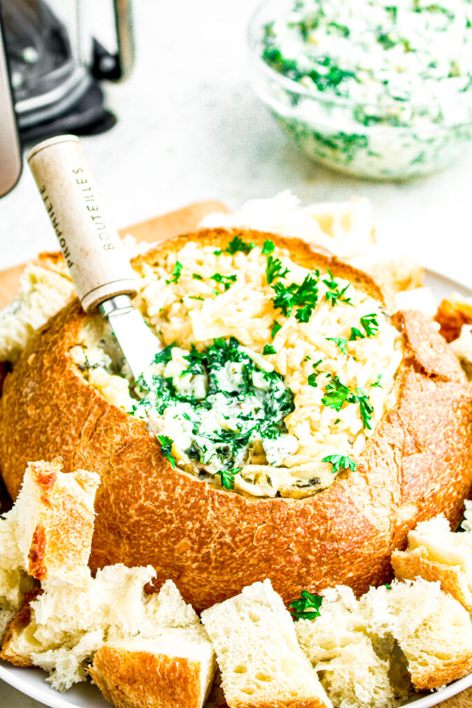 Close up overhead view of a round bread bowl filled with vegan artichoke dip with a knife sticking into it
