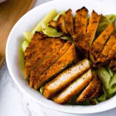 Overhead shot of a chipotle lime tofu cutlet in a bowl on avocado penne pasta