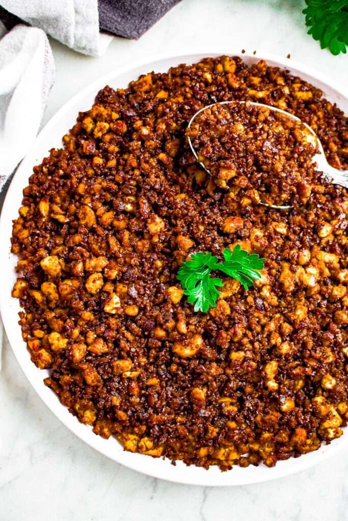 Overhead photo of vegan ground beef on a round white plate with a spoon digging into it