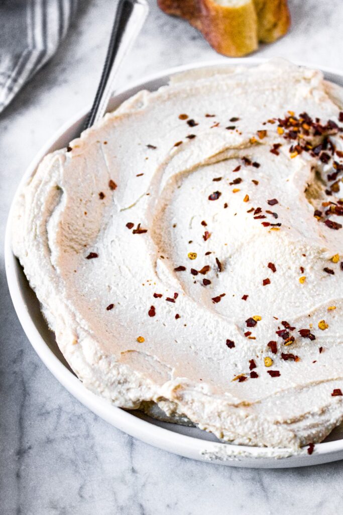 Head-on shot of a round plate with a schmear of tofu ricotta sprinkled with crushed red pepper flakes