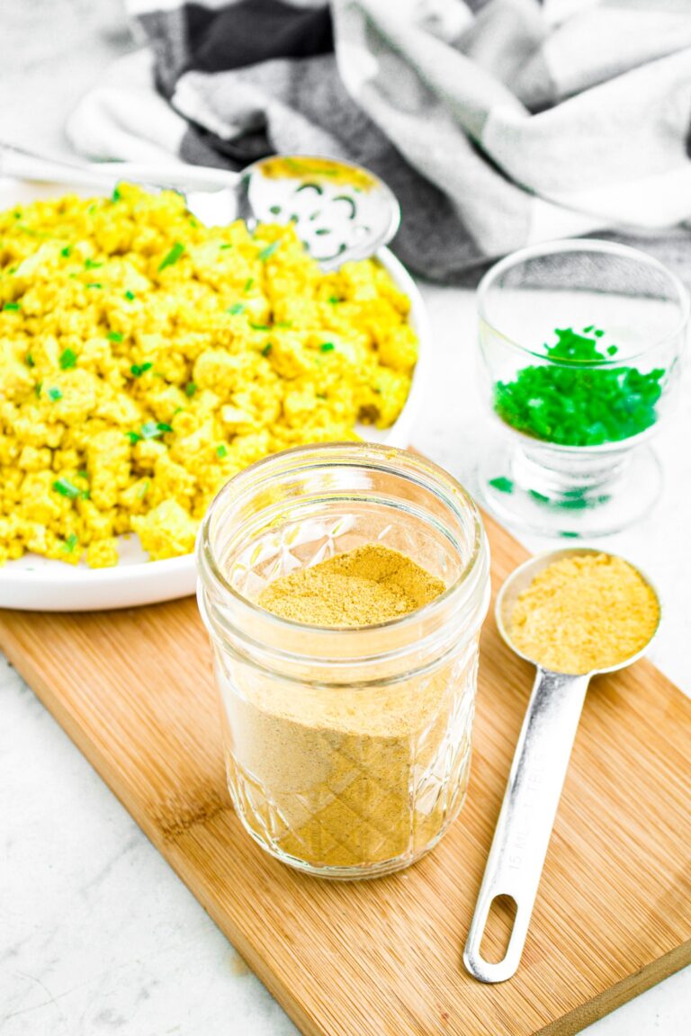 Head on photo of a small glass jar filled with tofu scramble seasoning next to a silver Tbsp filled with more scramble seasoning