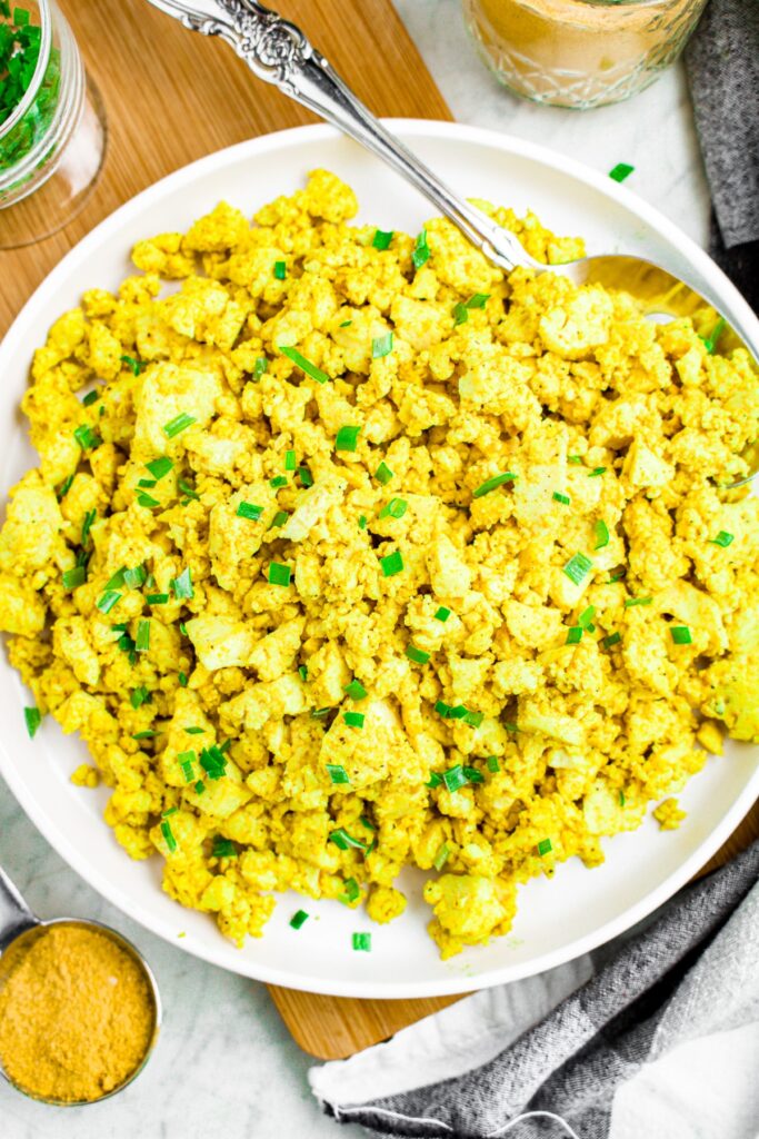 Overhead photo of a round white plate with a pile of scrambled tofu on it garnished with minced scallions