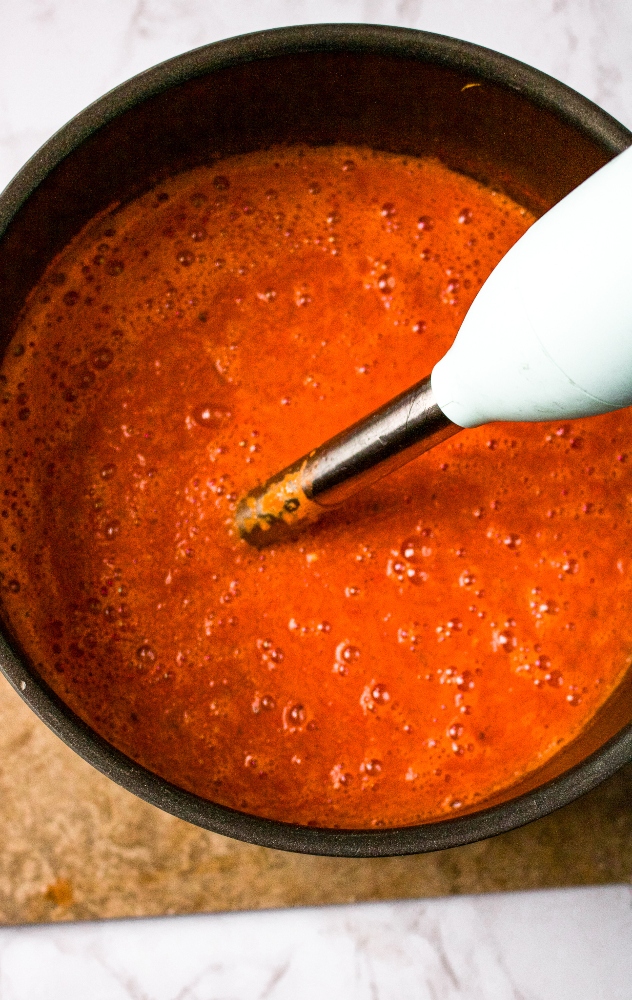 Overhead photo of an immersion blender blending tomato soup