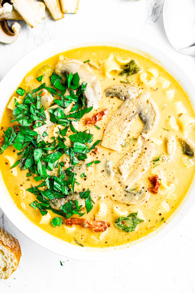 Overhead close up view of a round white bowl of creamy vegan Tuscan soup with one half of the bowl sprinkled with minced fresh herbs