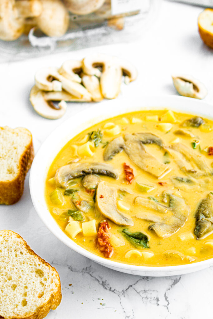 Overhead view of a round white bowl of creamy Tuscan mushroom soup next to two slices of bread