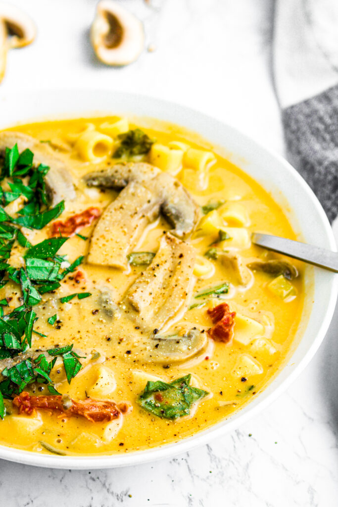 Overhead close up view of a spoon sticking into a round white bowl of creamy Italian mushroom and vegetable soup with fresh minced herbs on top