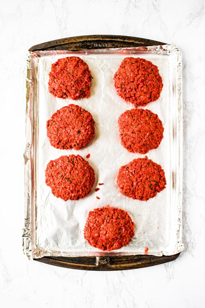 Overhead photo of 7 vegan burgers on a baking sheet before baking