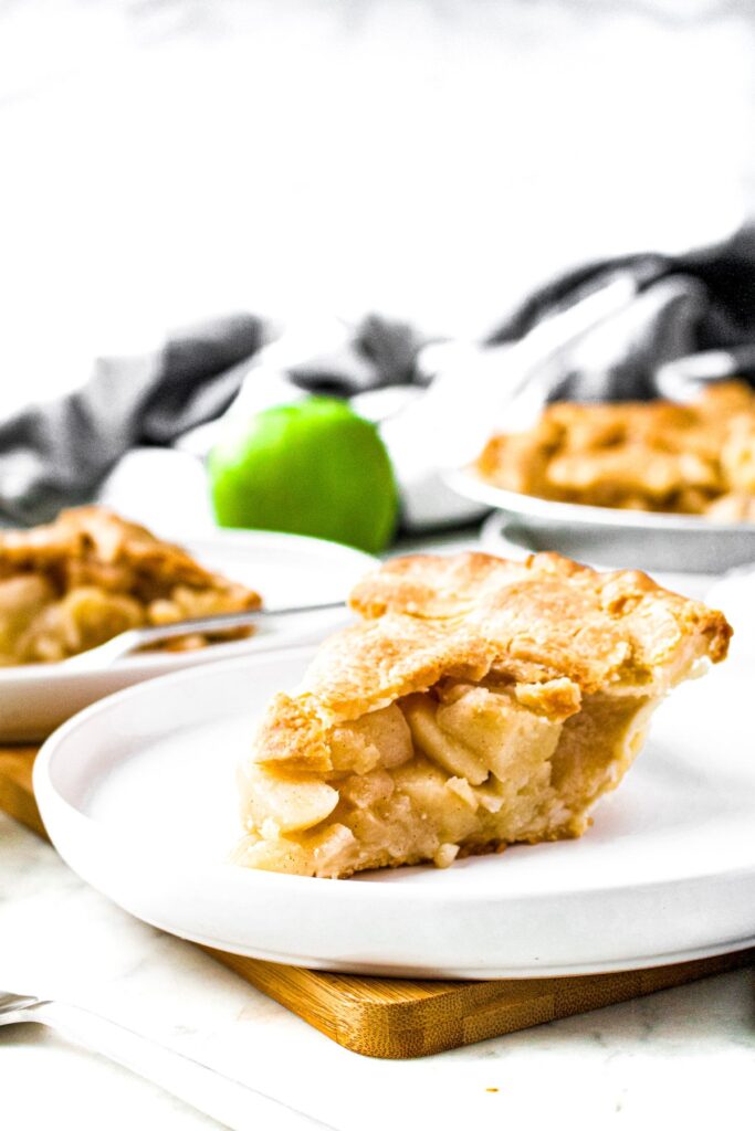 Head on photo of three slices of homemade apple pie on a round plate with a green apple in the background