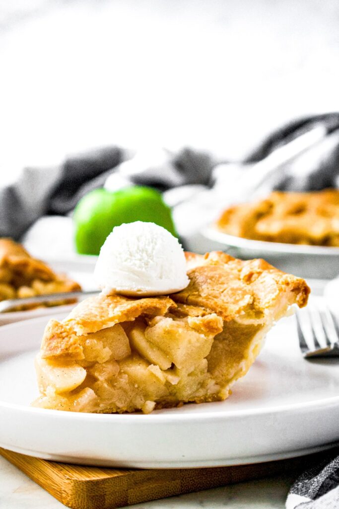 Head-on photo of a slice of vegan apple pie on a round white plate with another slice in the background