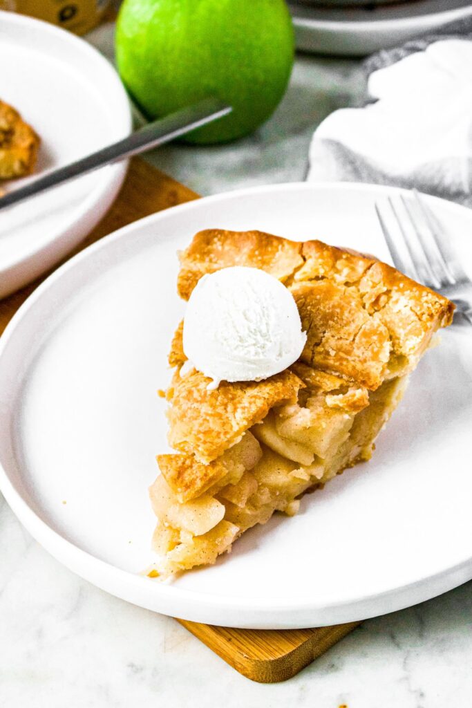 Overhead photo of a slice of vegan apple pie on a round white plate with a scoop of vanilla ice cream on top