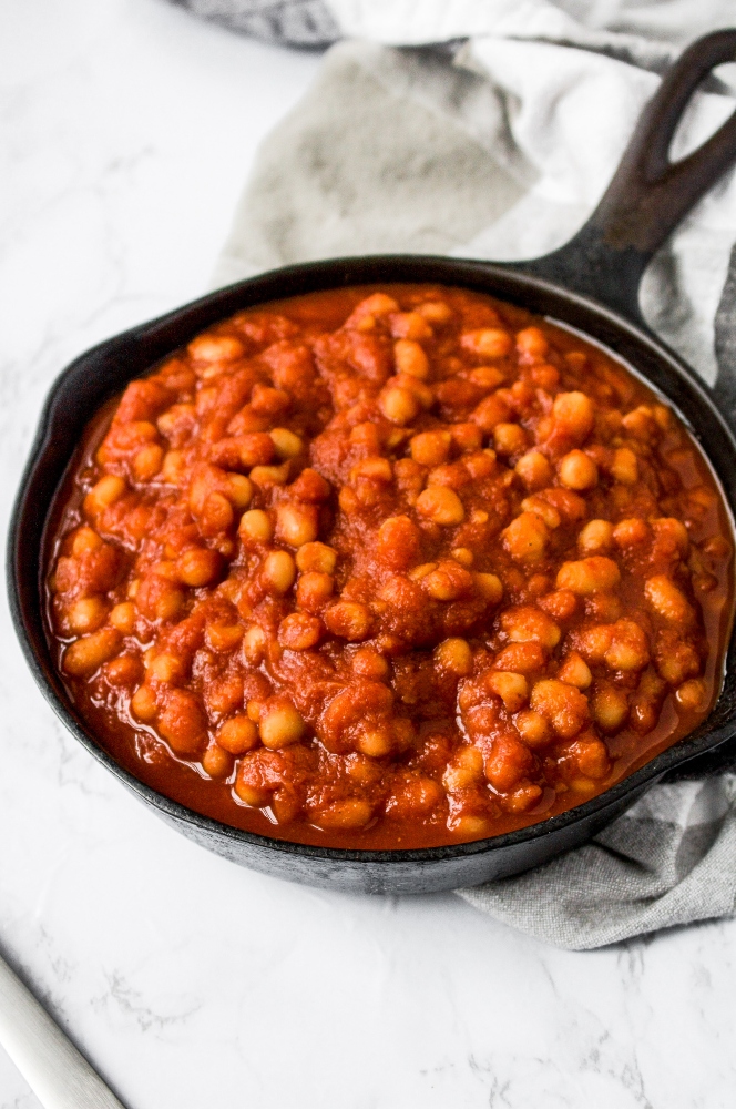 A skillet of healthy vegan baked beans with a black and white checkered napkin on a grey marble background. These easy vegan baked beans are the perfect summer BBQ side dish!