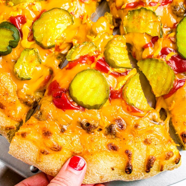 Overhead closup photo of a hand with red nail polish pulling a slice of vegan burger pizza out of the pie