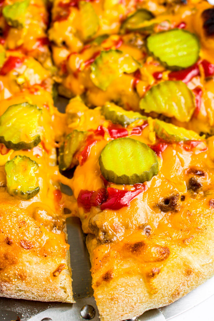 Close up overhead view of a slice of cheeseburger pizza topped with pickle chips