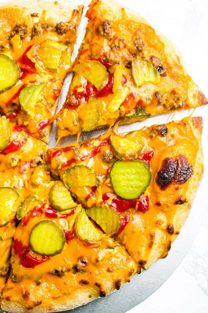 Overhead photo of the top right corner of a cheeseburger pizza with one slice pulled out