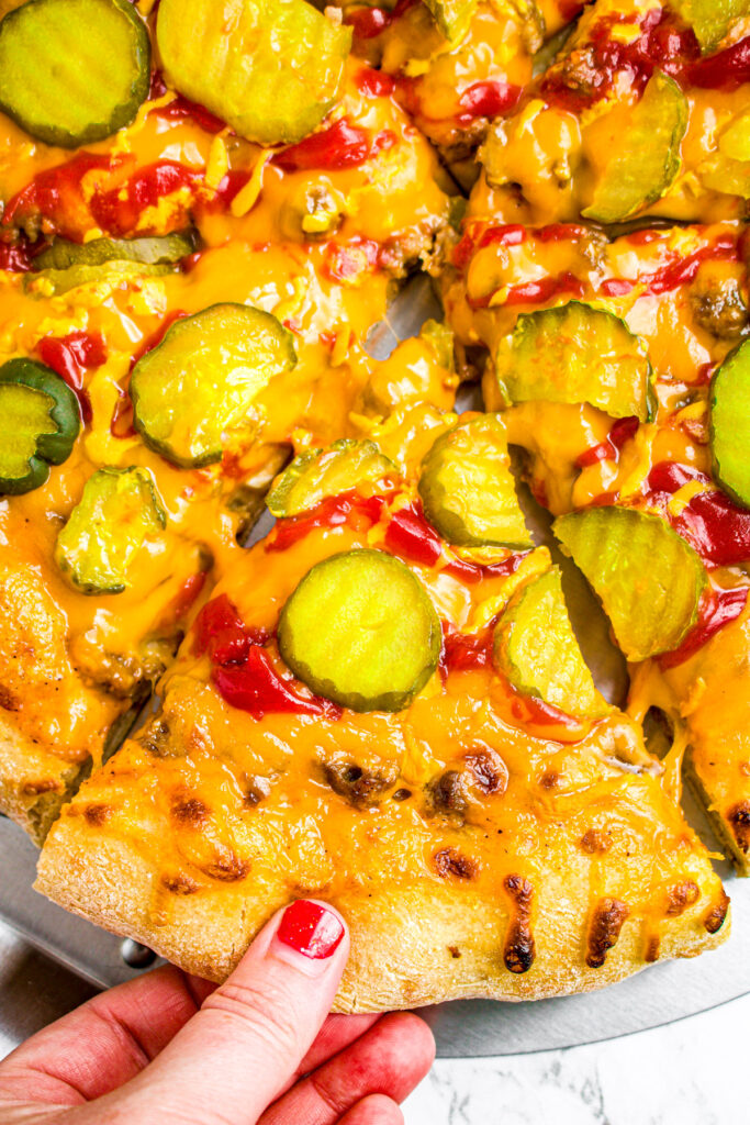 Close up overhead view of a vegan big mac pizza with a hand pulling one slice out
