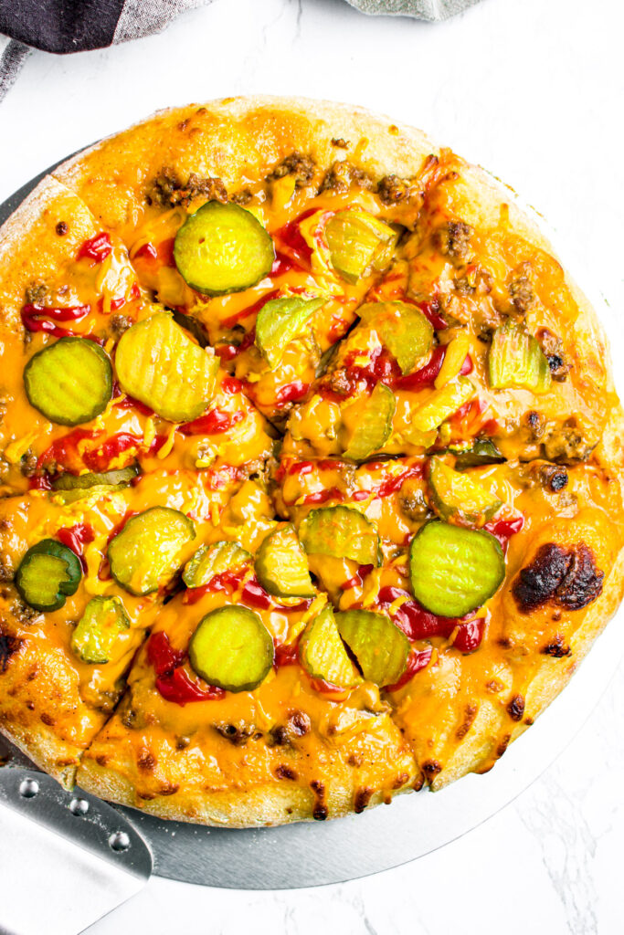 Overhead view of a sliced vegan Big Mac pizza topped with pickles and drizzled with ketchup