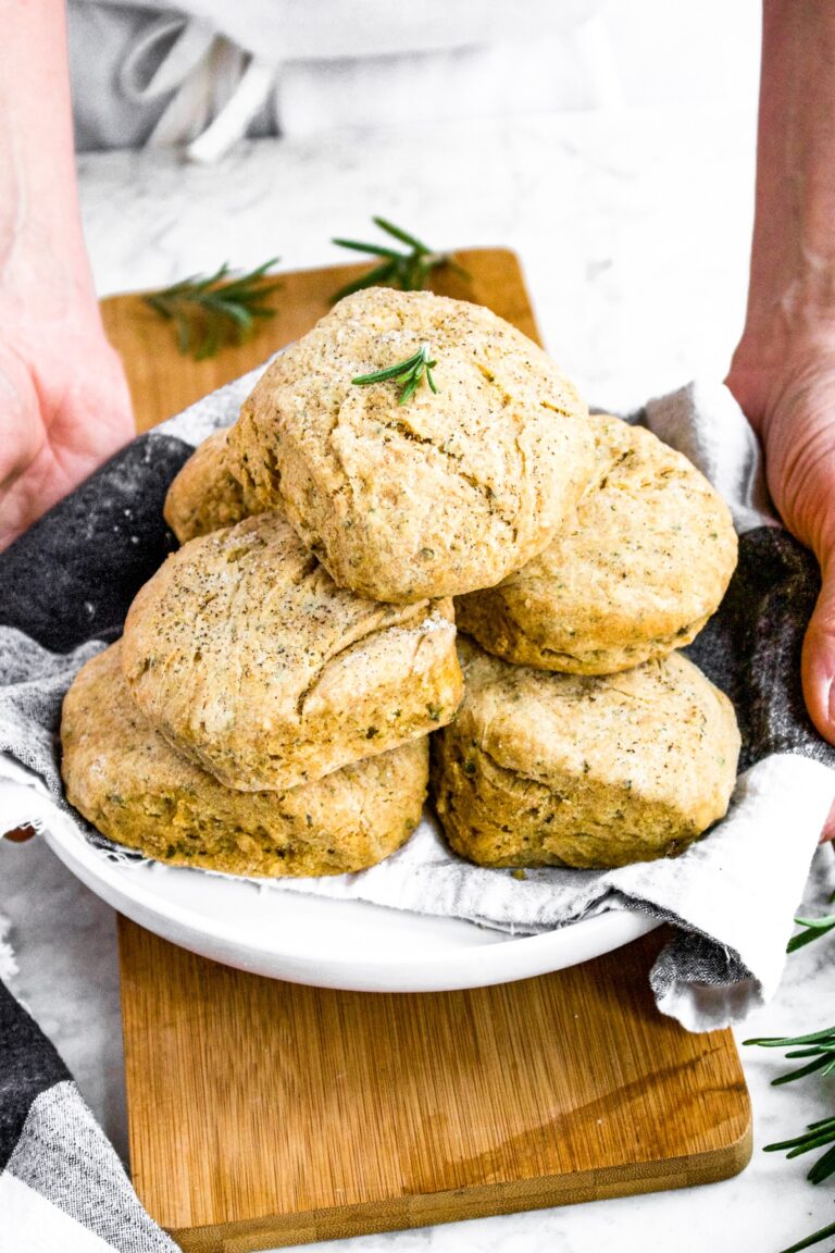 Head-on shot of a person in an apron setting a plate of dairy free biscuits on a table.