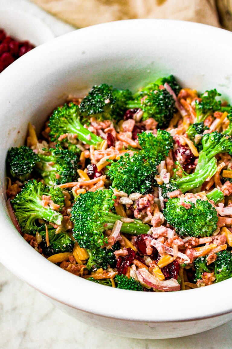 Overhead close up photo of a large white bowl filled with broccoli salad