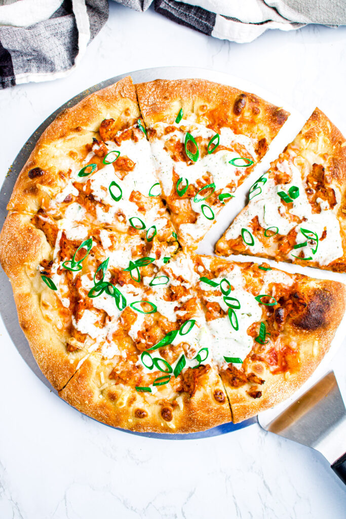 Overhead view of a pizza with buffalo soy curls, dill pickle ranch, and sliced scallions