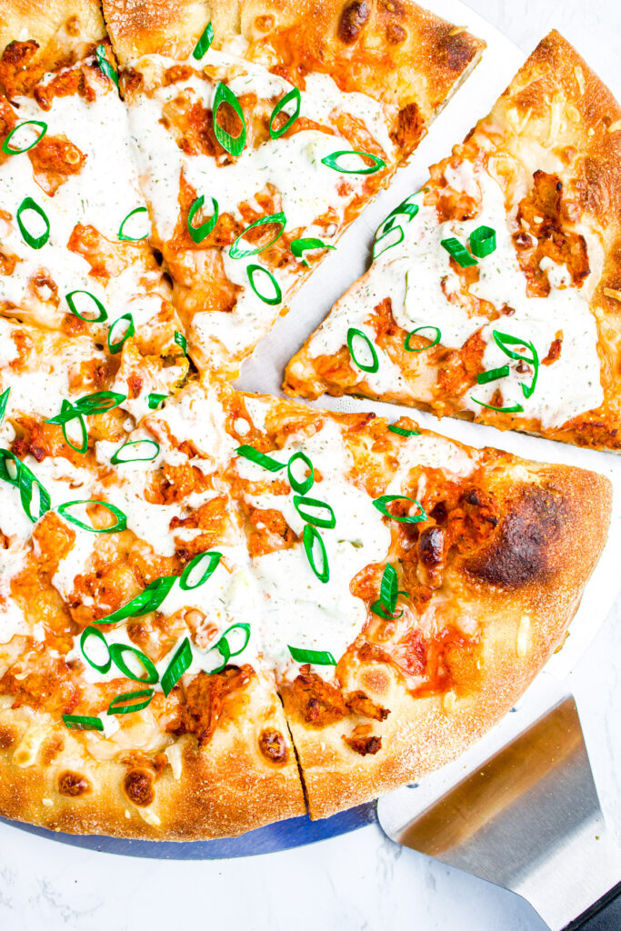 Zoomed in view of a meatless buffalo chicken pizza topped with scallions on a pizza peel