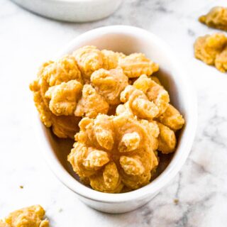 A head-on shot of flower-shaped vegan cheese straws arranged in a white oval shaped dish. There is a matching dish also filled with cheese straws in the background and more dairy free cheese straws around the two dishes.