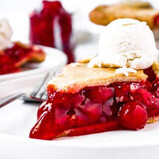 Close up head-on photo of a slice of cherry pie with vegan ice cream on top